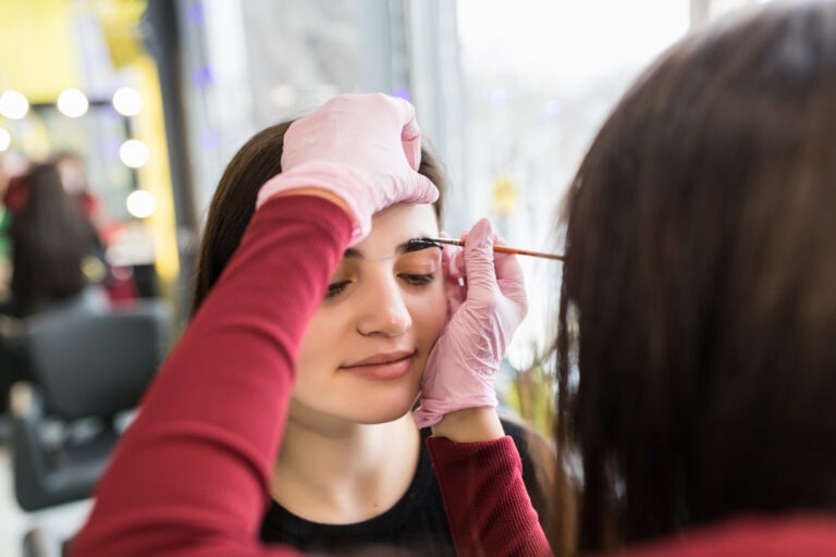 female master put eyebrow paint in beauty salon during make-up procedure